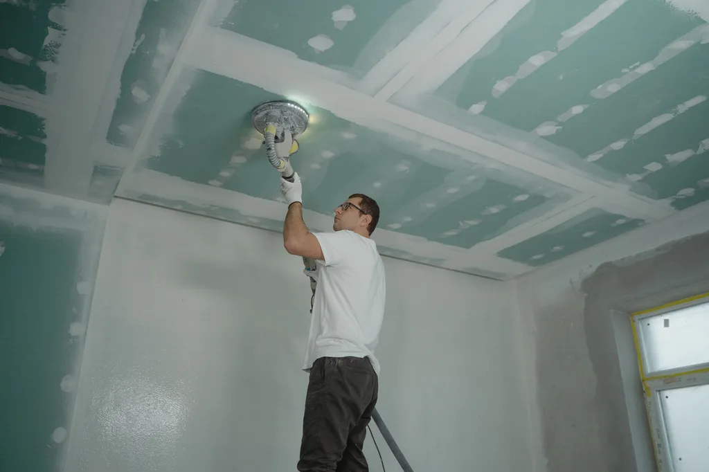 Drywall finisher sanding a taped ceiling seam